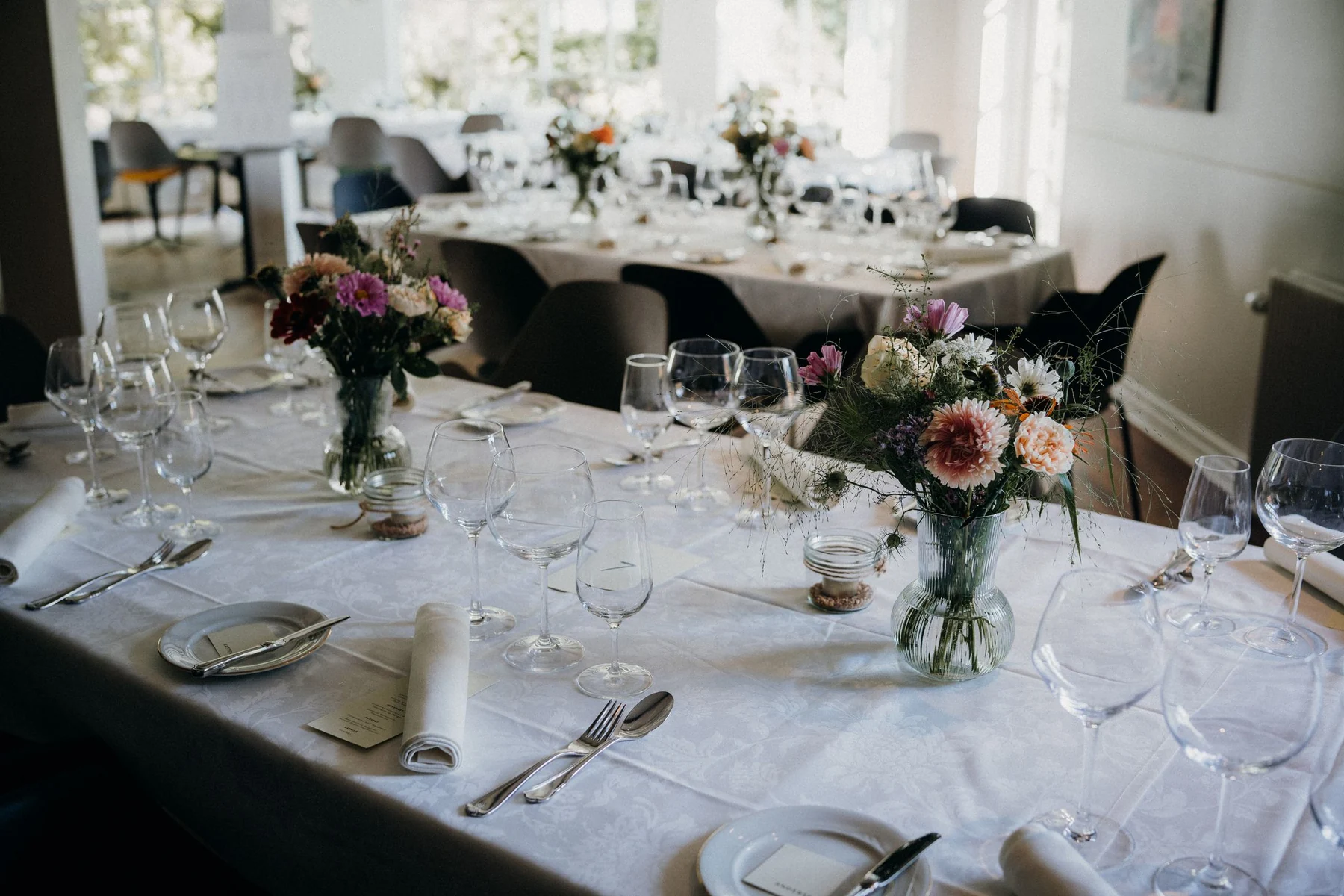 Blumen und Gläser auf gedeckten Hochzeitstischen